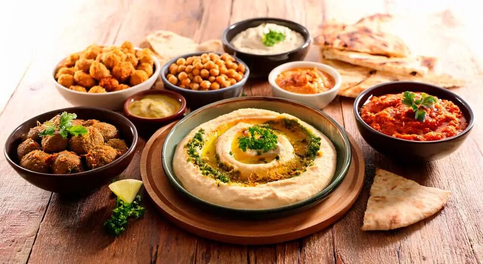 Mesa de culinária árabe da YOFAH para eventos, com hommus, kibes, grão-de-bico e pães